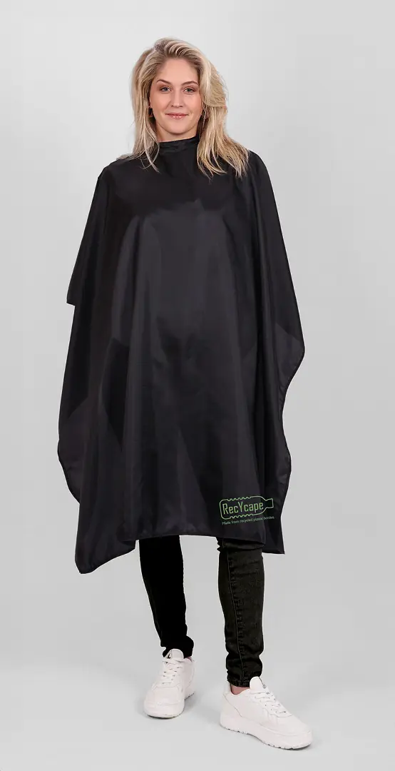 Frau in einem schwarzen Umhang von TrendDesign, steht vor einer weißen Wand.